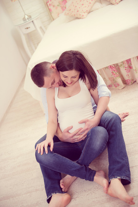 Ein junges Paar sitzt umschlungen im Schlafzimmer und freut sich auf die baldige Geburt seines Kindes.