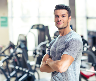 Sportlicher Mann im Fitnessstudio Ein sportlicher Mann steht mit verschränkten Armen im Fitnessstudio.